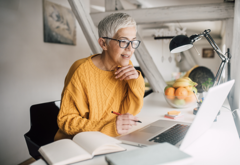 elder lady with glasses at a desk in an office looking at a computer