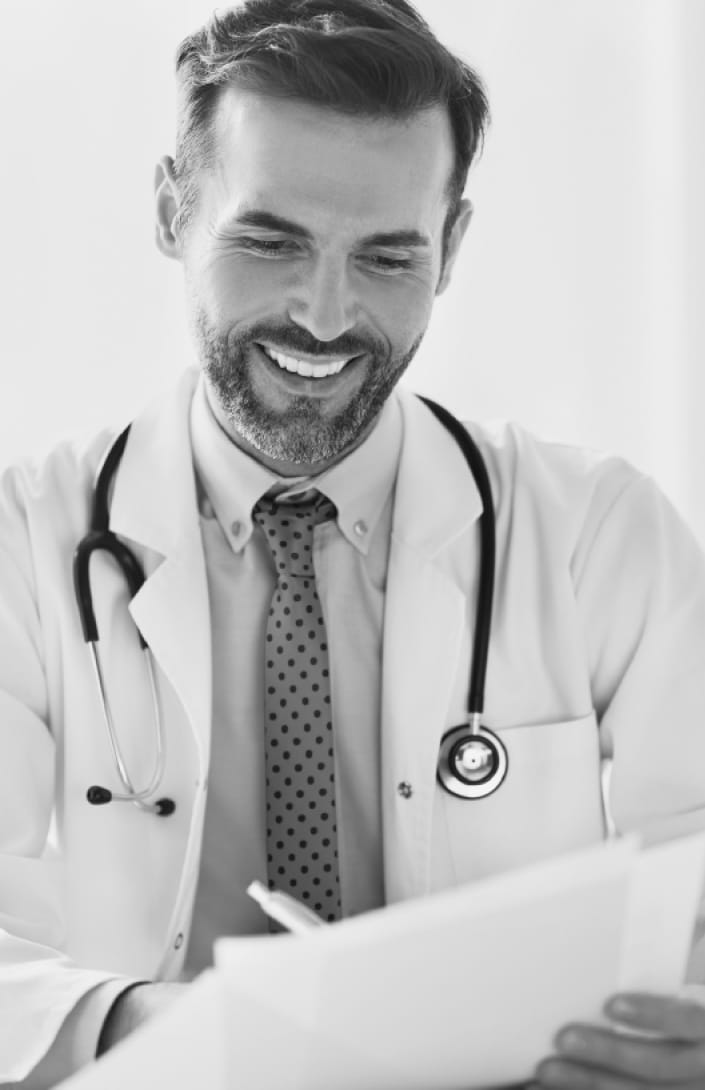 doctor with beard smiling down, wearing a white medical coat and stethoscope