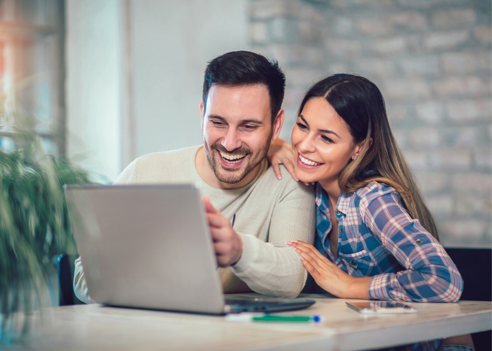 A young adult couple at home smiling at a laptop together 