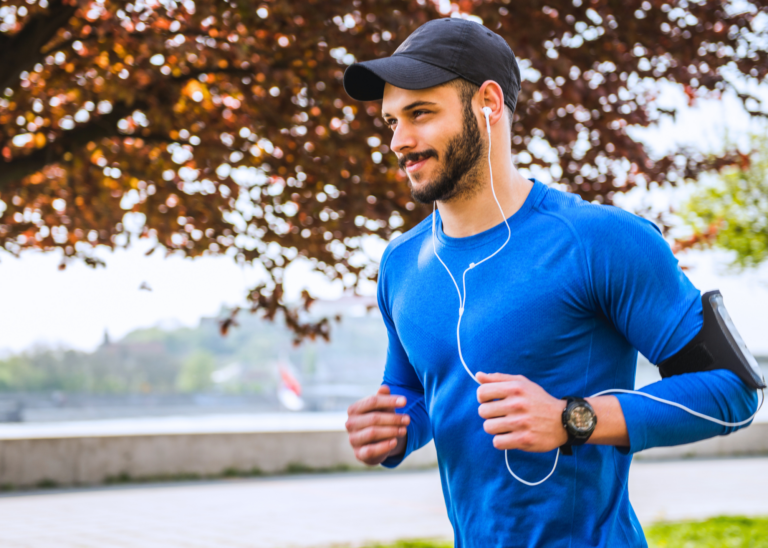 bearded athletic man with headphones on jogging outside with trees and a river in the background