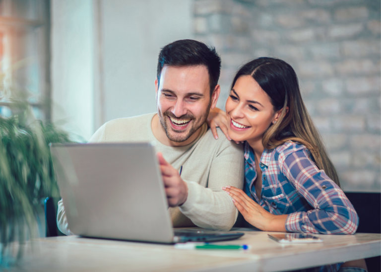 A young adult couple at home smiling at a laptop together